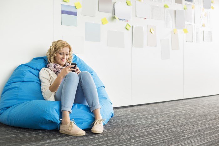 Blonde girl sitting on a beanbag chair and using a smartphone