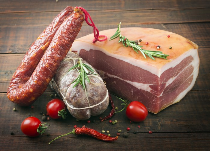 Meat products, sausages, tomatoes, and chili pepper on wooden table