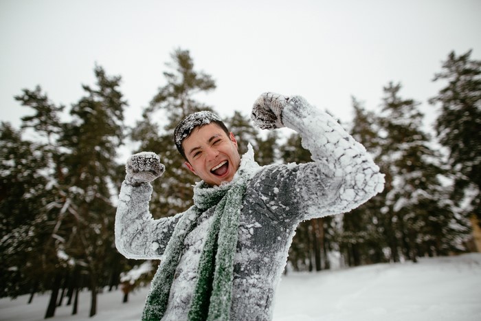 Man covered in snow celebrating in a forest