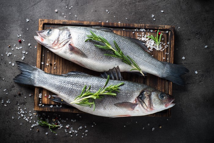 Two raw fish with rosemary and salt on a cutting board
