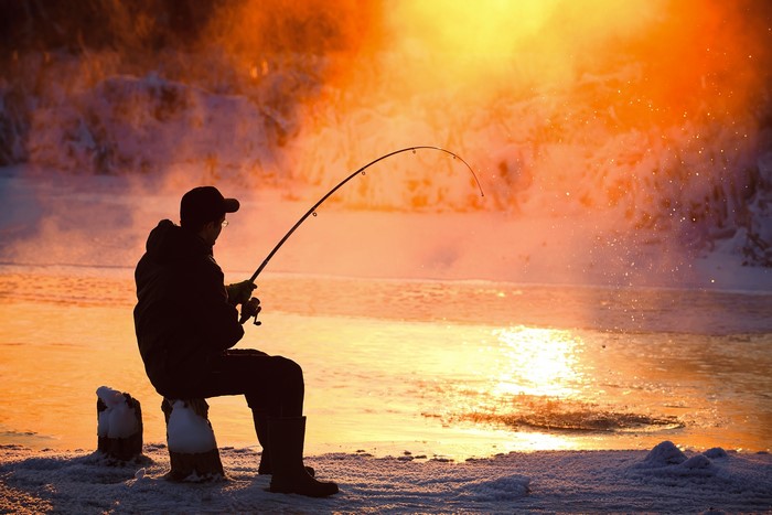 Man fishing in winter at sunset