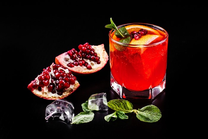 Pomegranate cocktail with ice and mint on black background