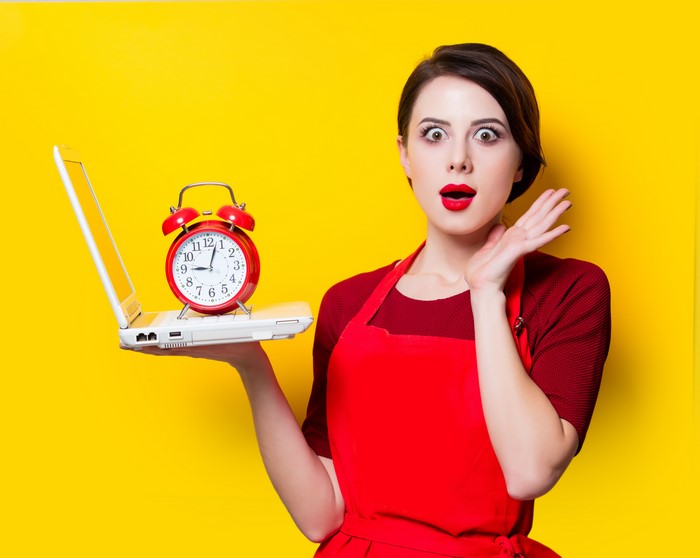 Woman in red holding a laptop with an alarm clock