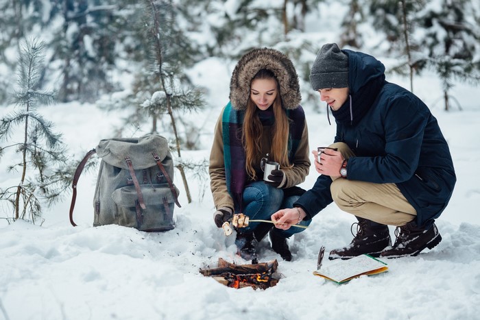 Couple roasting marshmallows over a bonfire in winter forest