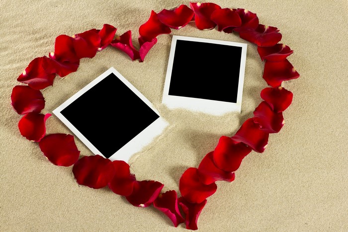 Heart shape made of rose petals with two photo frames on sand