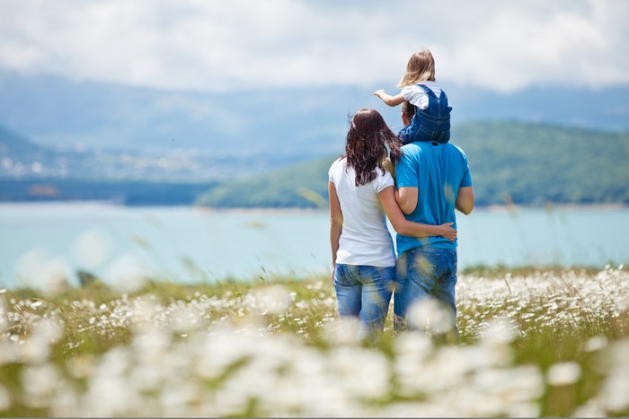 Family with daughter on shoulders overlooking a lake