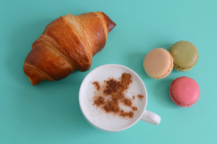 Croissant, cappuccino, and macarons on a teal background