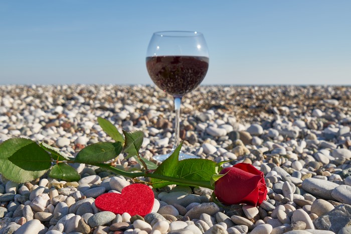 Red rose and wine glass on a pebble beach