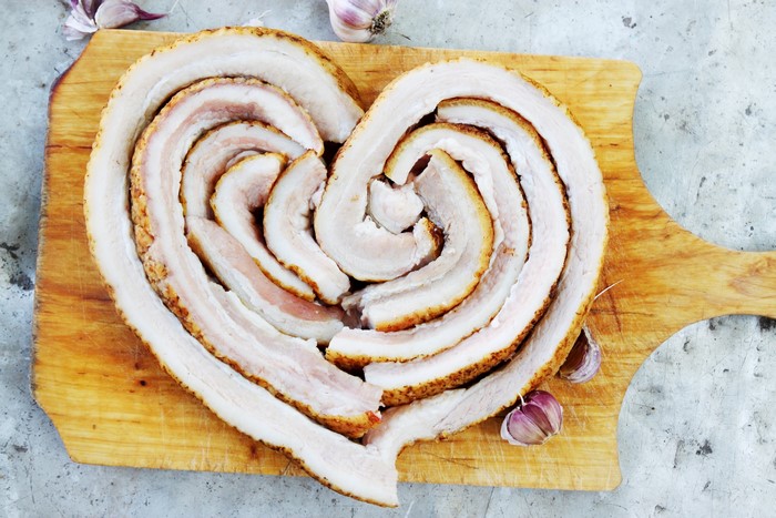 Salo in a heart shape on a cutting board with garlic