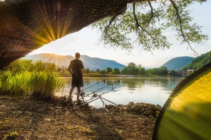 Man fishing by lake at sunrise with tent