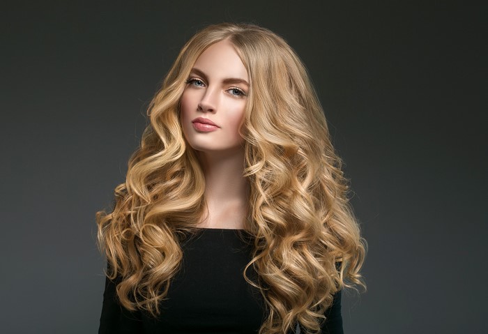 Blonde woman with curly hair on gray background