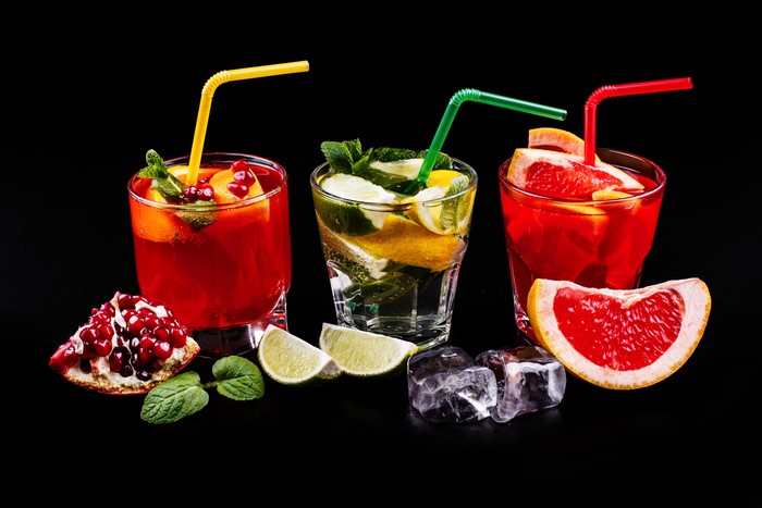 Three cocktails with pomegranate, grapefruit, and lime on black background