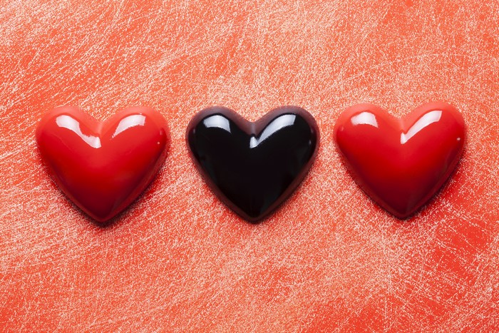 Three heart-shaped candies on a textured red surface