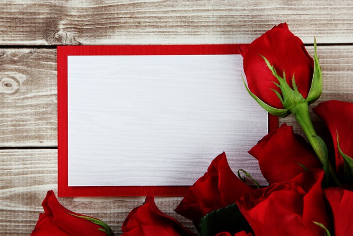 Red roses and blank greeting card on wood