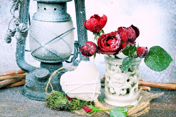 Roses in a vase next to a snow-covered kerosene lamp