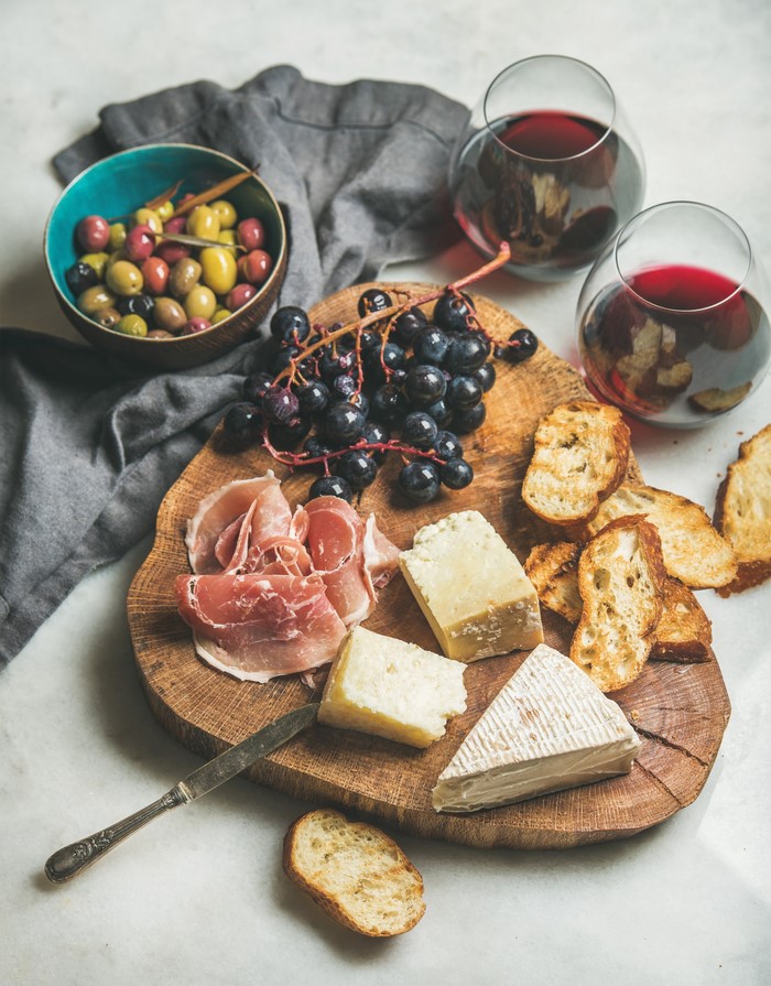 Cheese, Ham, Grapes, Olives, Bread, and Wine on a Cutting Board