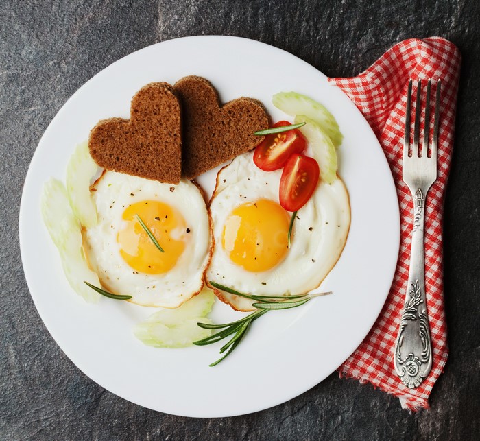 Two heart-shaped toasts with fried eggs and cherry tomatoes on a plate
