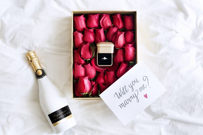 Champagne bottle, roses, ring box, and 'Will you marry me?' card