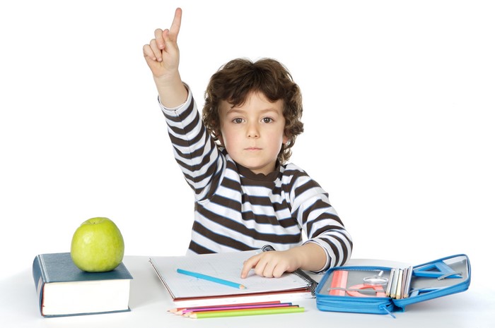 Boy with hand raised at desk with school supplies