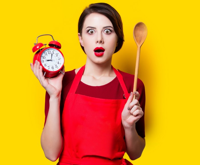 Woman in red apron holding alarm clock and spoon