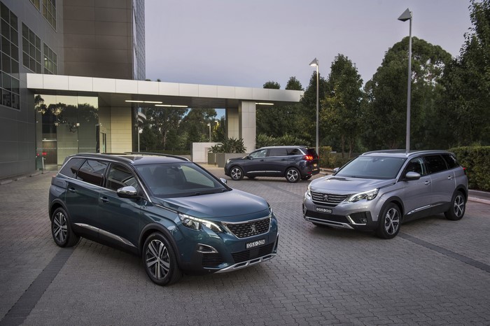 Three Peugeot 5008 SUVs parked outside a modern building