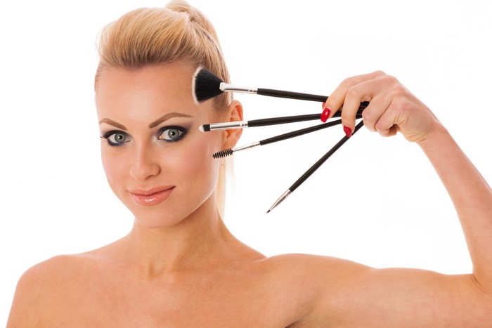Blonde woman with makeup brushes on white background