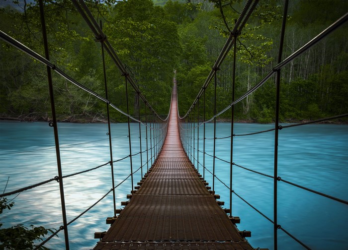 Suspension bridge over a turquoise river in a forest