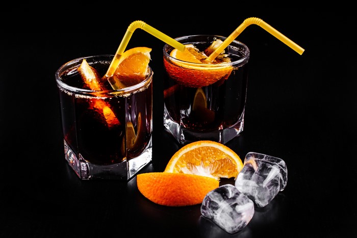 Two cocktails with orange slices and straws on black background