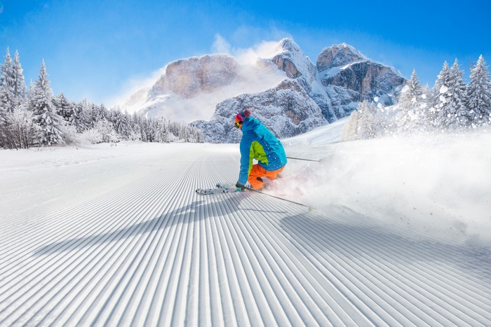 Skier in colorful ski suit on a groomed slope with mountains