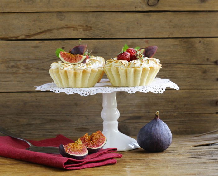 Two fig and strawberry tarts on a cake stand