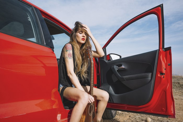 Woman with guitar sitting in red car