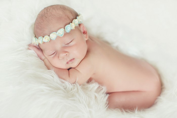 Newborn baby sleeping on white fur with flower crown