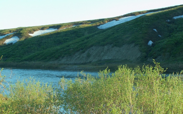 River flowing past a grassy hill with snow patches