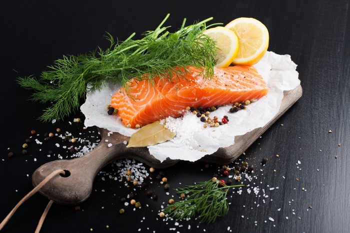 Salmon fillet with dill, lemon, and spices on a cutting board
