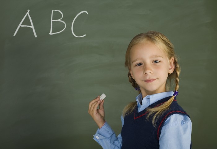 Girl holding chalk in front of ABC on a chalkboard