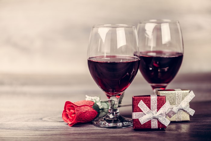 Two glasses of red wine with rose and gifts