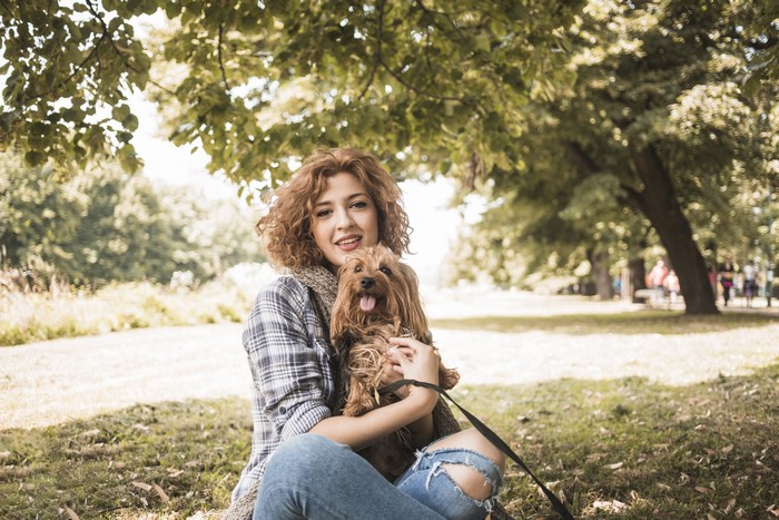 Woman with curly brown hair holding a dog in a park