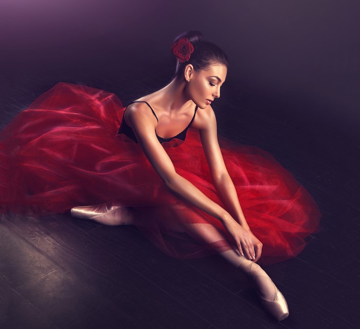 Ballerina in red tutu tying pointe shoes