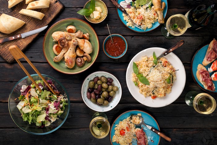 Table setting with roast chicken, salad, olives, bread, and wine