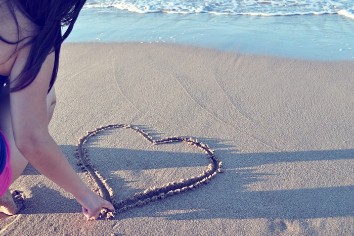 Girl drawing a heart in the sand on the beach