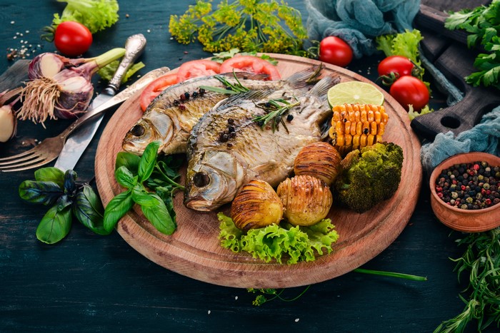 Whole roasted fish with potatoes, broccoli, and corn on a cutting board