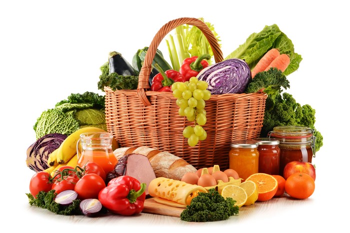 Wicker basket filled with fresh vegetables, fruits, bread, and eggs