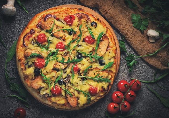 Pizza with chicken, tomatoes, olives, and arugula
