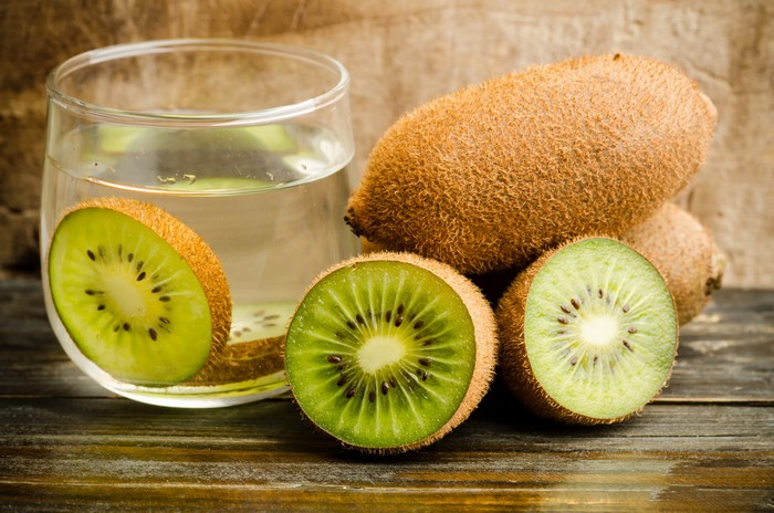 Kiwi slices and whole kiwis next to a glass of kiwi juice