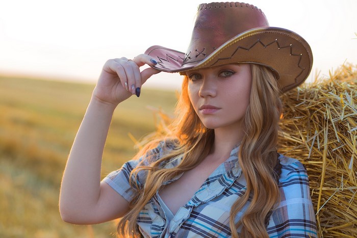 Woman in cowboy hat and plaid shirt near hay bale