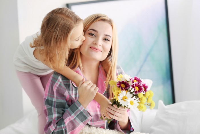 Girl kissing mother holding flowers