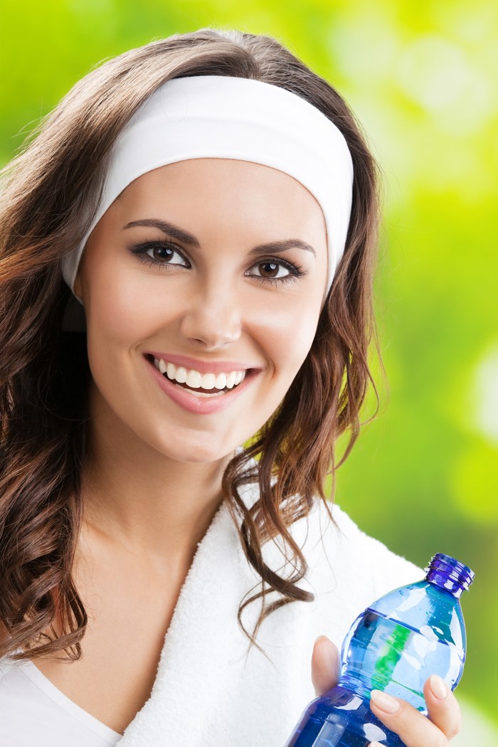 Woman with brown hair wearing a white headband holding a water bottle