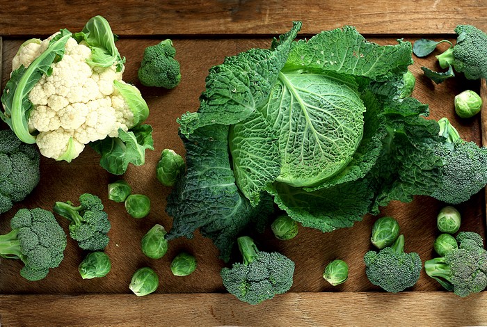 Assortment of fresh vegetables including cauliflower, broccoli, cabbage, and Brussels sprouts on a wooden surface.
