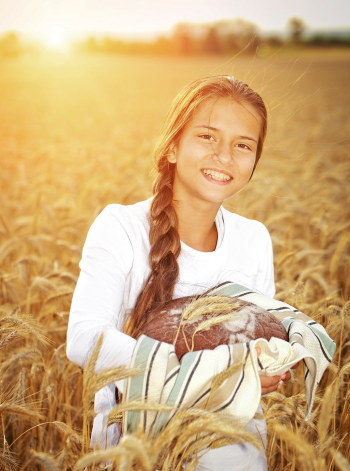 Girl holding bread in a wheat field at sunset