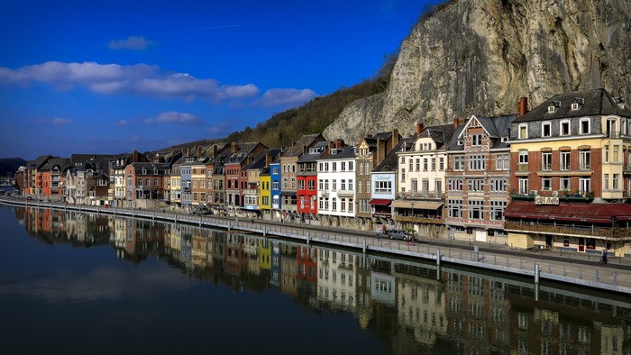 Colorful houses along the river in Dinant, Belgium with a large crag.